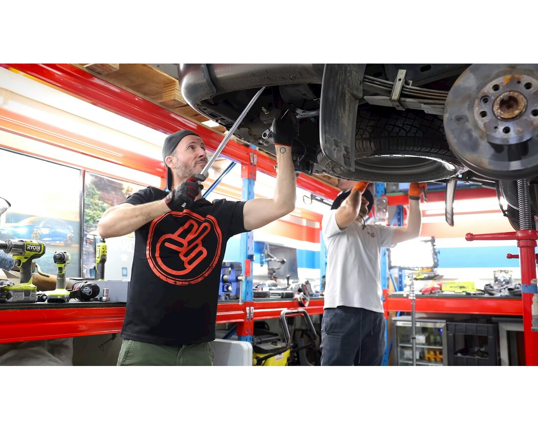 Two mechanics working under a vehicle on a lift in the Main Street Automotive shop